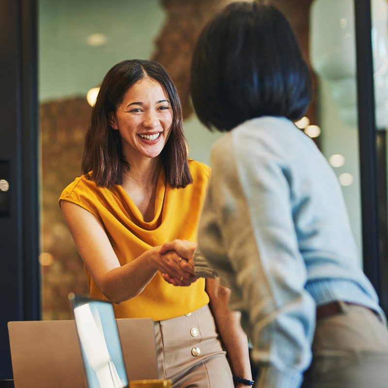 Lady in yellow top smiling shaking hands with another lady